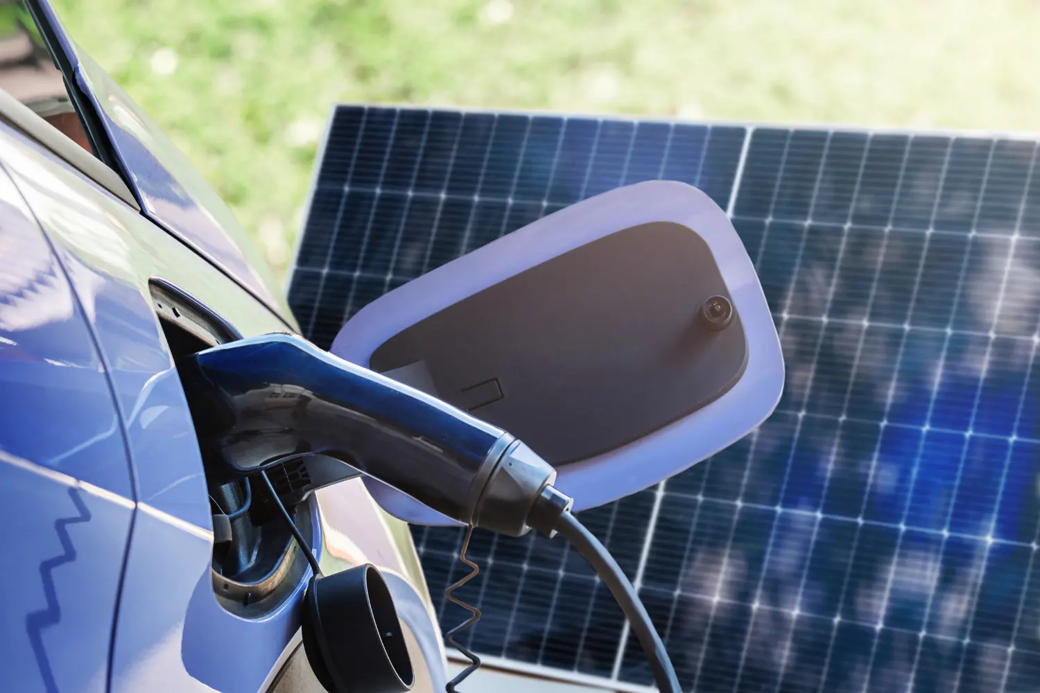 Ladestecker in blauem Elektroauto, im Hintergrund ein Solarpanel im Freien