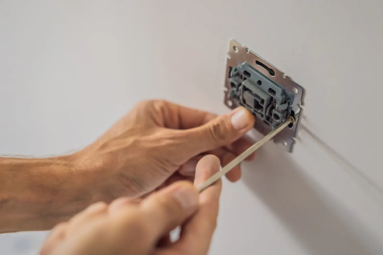 Elektriker montiert einen Steckdoseneinsatz mit einem Schraubenzieher an der Wand.